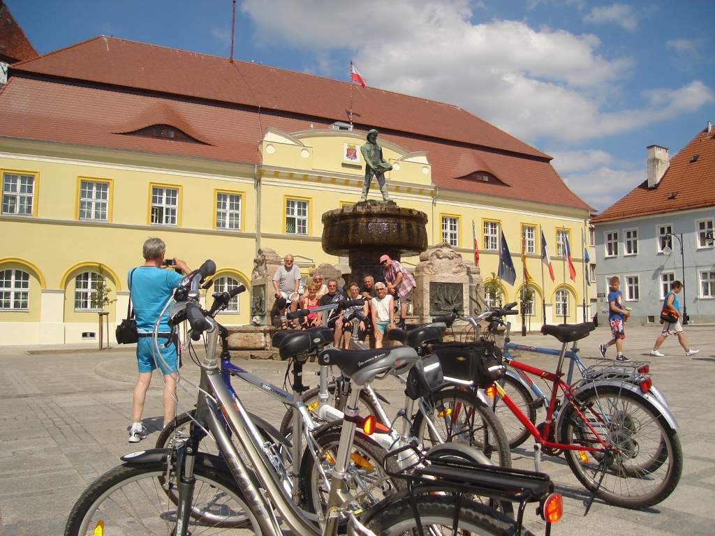 Turnus Rehabilitacyjny Darłówka 2011 r. Uczestnicy wycieczki rowerowej pozują do zdjęcia pod fontanną na miejskim rynku.